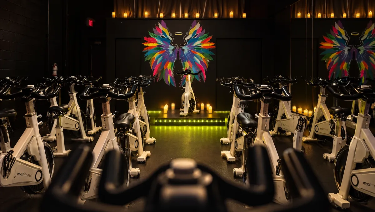 The room at Culture of Sweat lit by candles, thirteen bikes facing the wings on the wall